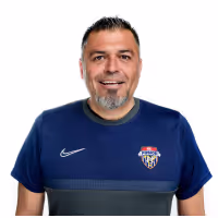 Man with short dark hair and a goatee wearing a blue Nike sports shirt with a crest logo.