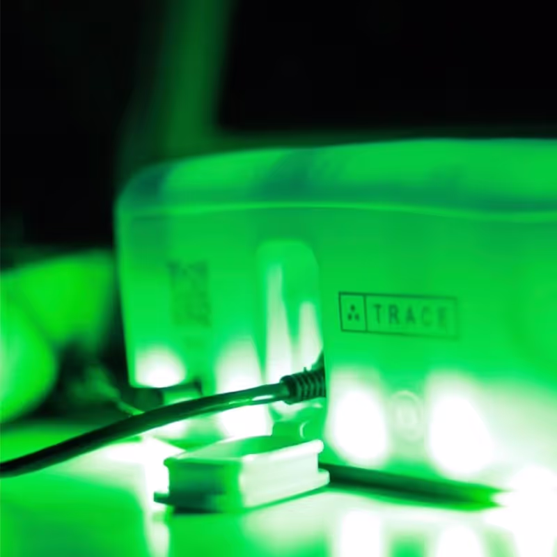 Close-up of the rear part of a device labeled TRACER with a cable plugged in, illuminated by green light.