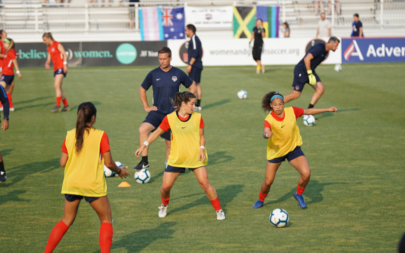 Soccer Possession Drill Warm-Up Women soccer players in yellow training bibs run a possession drill while coaches watch on a grass field