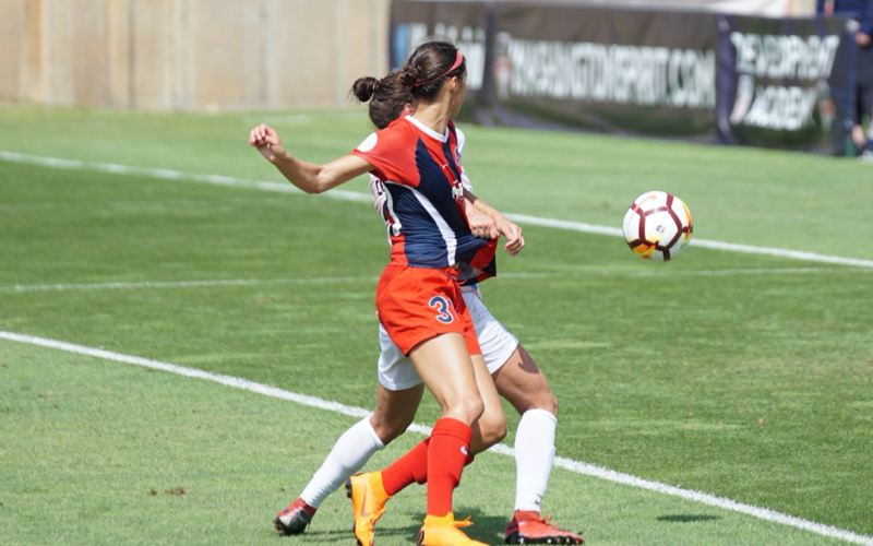 Two women soccer players battle for the ball near a Washington Spirit sideline banner