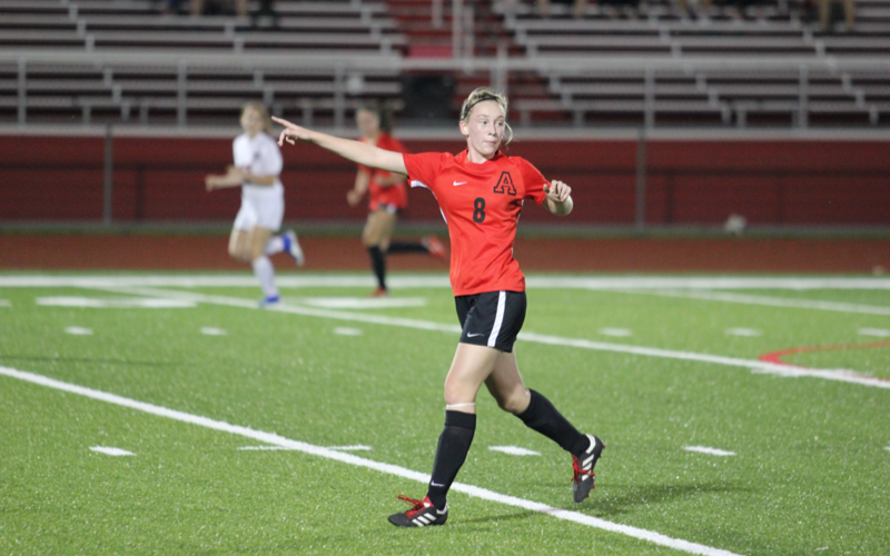 Female soccer player in a red number 8 jersey points and directs teammates during a night match