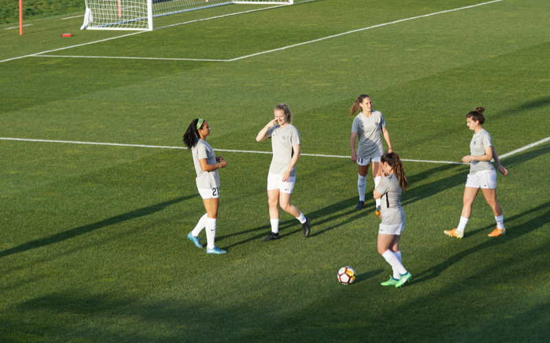 Team Warming Up Near Goal Women soccer players in gray training kits warm up near the goal, one dribbling a ball