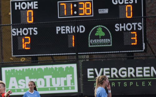 Stadium scoreboard reads 0-0 at 71:38 above AstroTurf and Evergreen Sportsplex banners with players below