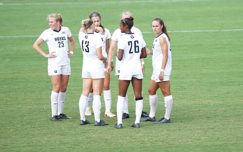Georgetown Hoyas women's soccer players in white kits gather on the field during a stoppage