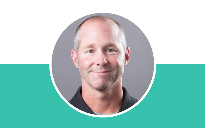Headshot of a smiling man with short gray hair on a teal and white background