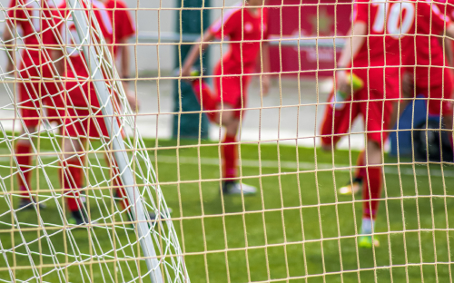 Players Seen Through Goal Net View through a goal net of youth players in red kits warming up on the field