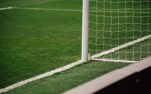 Close-up of a white goalpost base and net meeting the sideline on a grass field