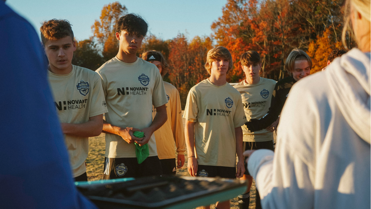 Team Gathered Around Coach Boys team in Novant Health jerseys gather around a coach on the field at golden hour