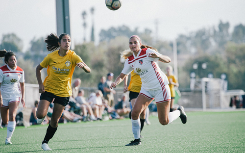 Sprinting After The Ball Women soccer players in yellow and white kits sprint after a ball in the air during a match