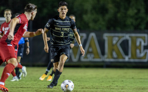 Wake Forest player number 3 in black kit dribbling past red-shirted opponents during a night match
