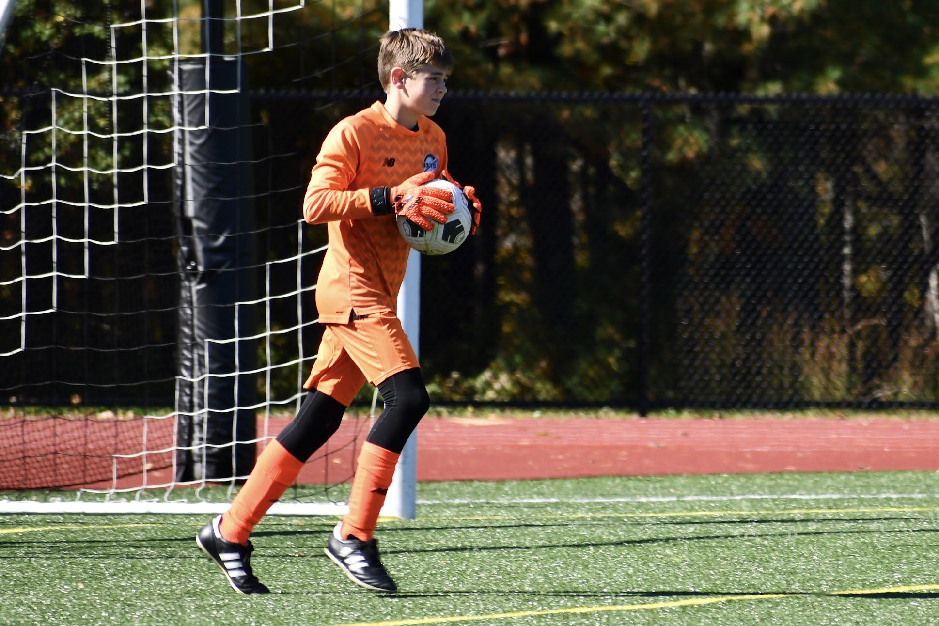 Young Goalkeeper Holding Ball Young goalkeeper in orange kit holding the ball in front of the net on a turf field