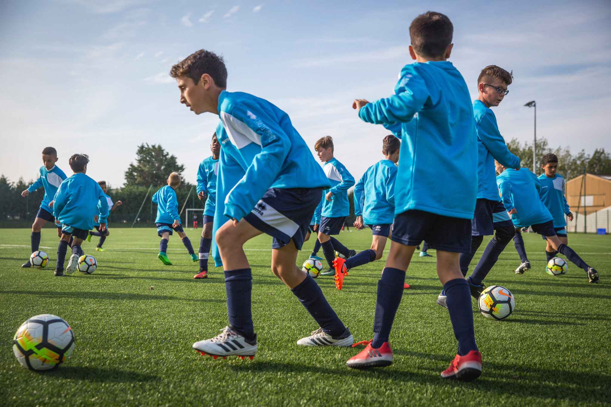 Youth Team Training Drills Group of young boys in blue training tops practicing ball drills across a turf field