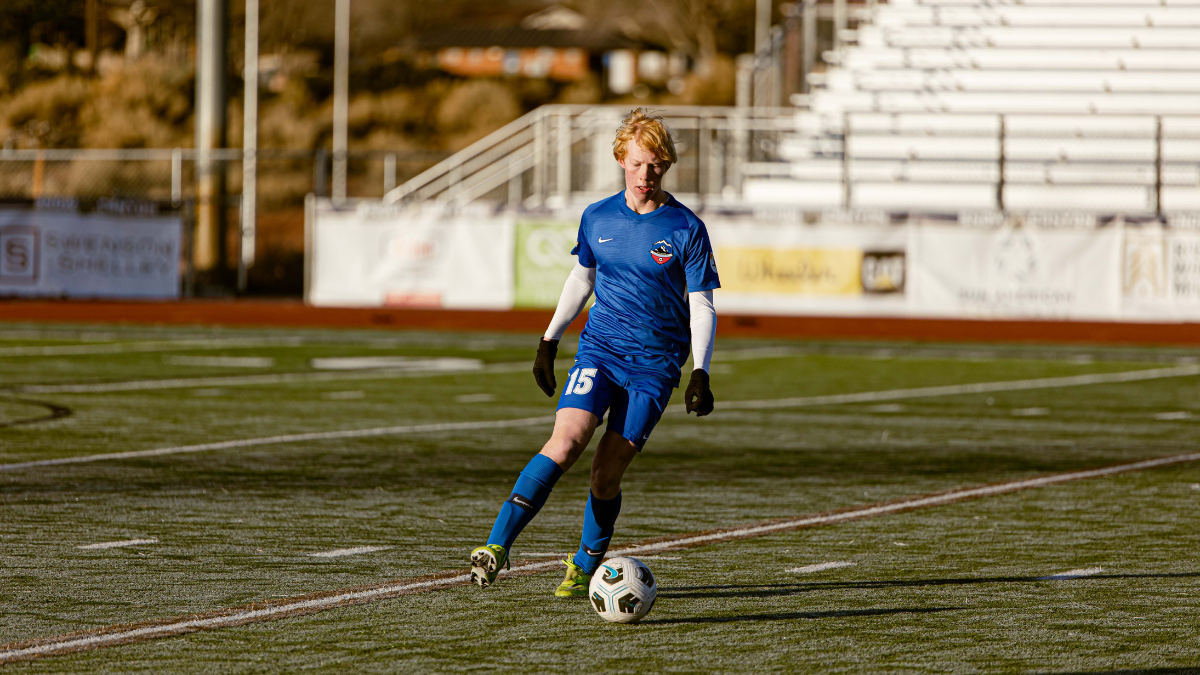 Player Dribbling In Sunlight Youth player number 15 in blue kit dribbling on a turf field in winter sunlight