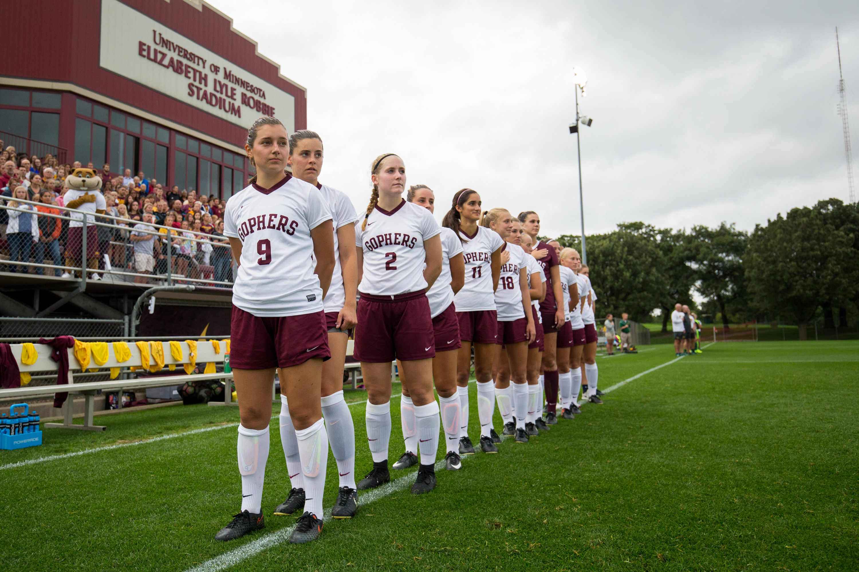 University of Minnesota Gophers women's soccer players stand in a line along the field before a match.