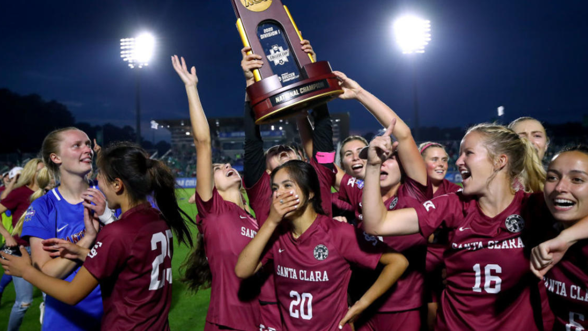 Santa Clara Championship Celebration Santa Clara women's players in maroon kits lift the NCAA Division I championship trophy at night.