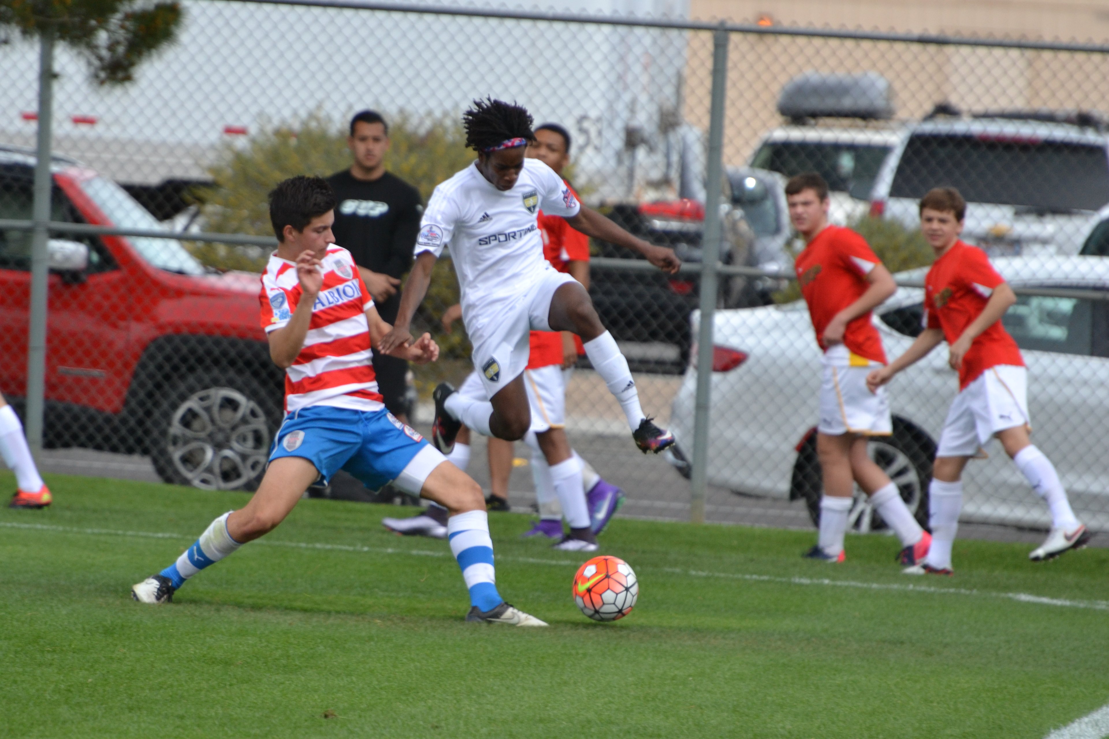 Teens Contest A Loose Ball Teen boy in white leaps over the ball as a defender in red stripes challenges during a soccer match.