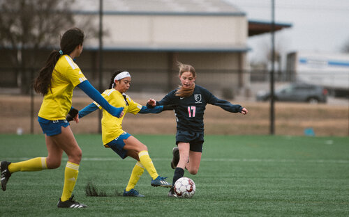 Girls Defending On Field Girls soccer match with a navy number 17 dribbling the ball past two defenders in yellow