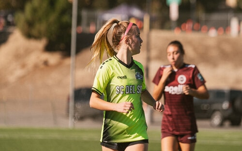 Player Scanning The Field Female player in a green SC Del Sol kit jogging on the field with an opponent behind her