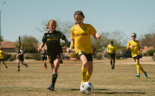 Young Girl Dribbling Ball Young girl in a yellow kit dribbling the ball past a defender during a sunny youth soccer game