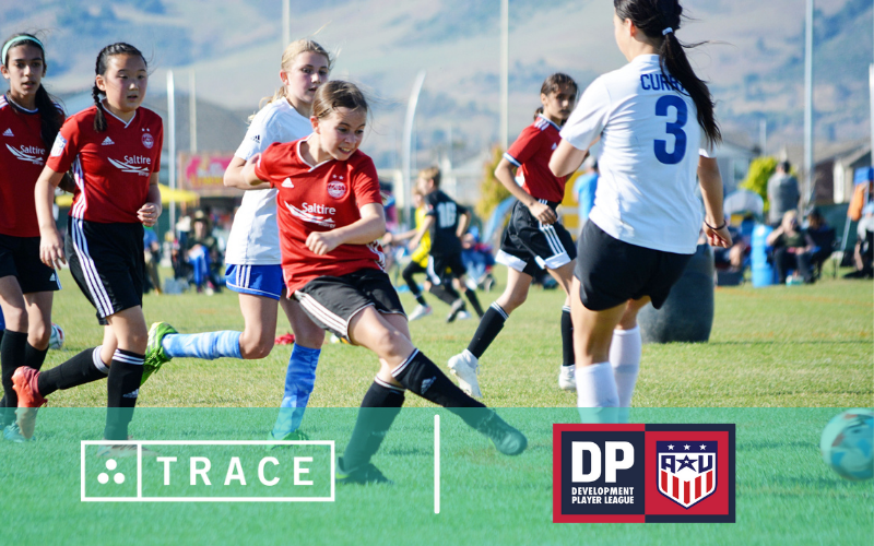 Youth girls soccer match, a red-jersey player striking the ball; Trace and Development Player League logos