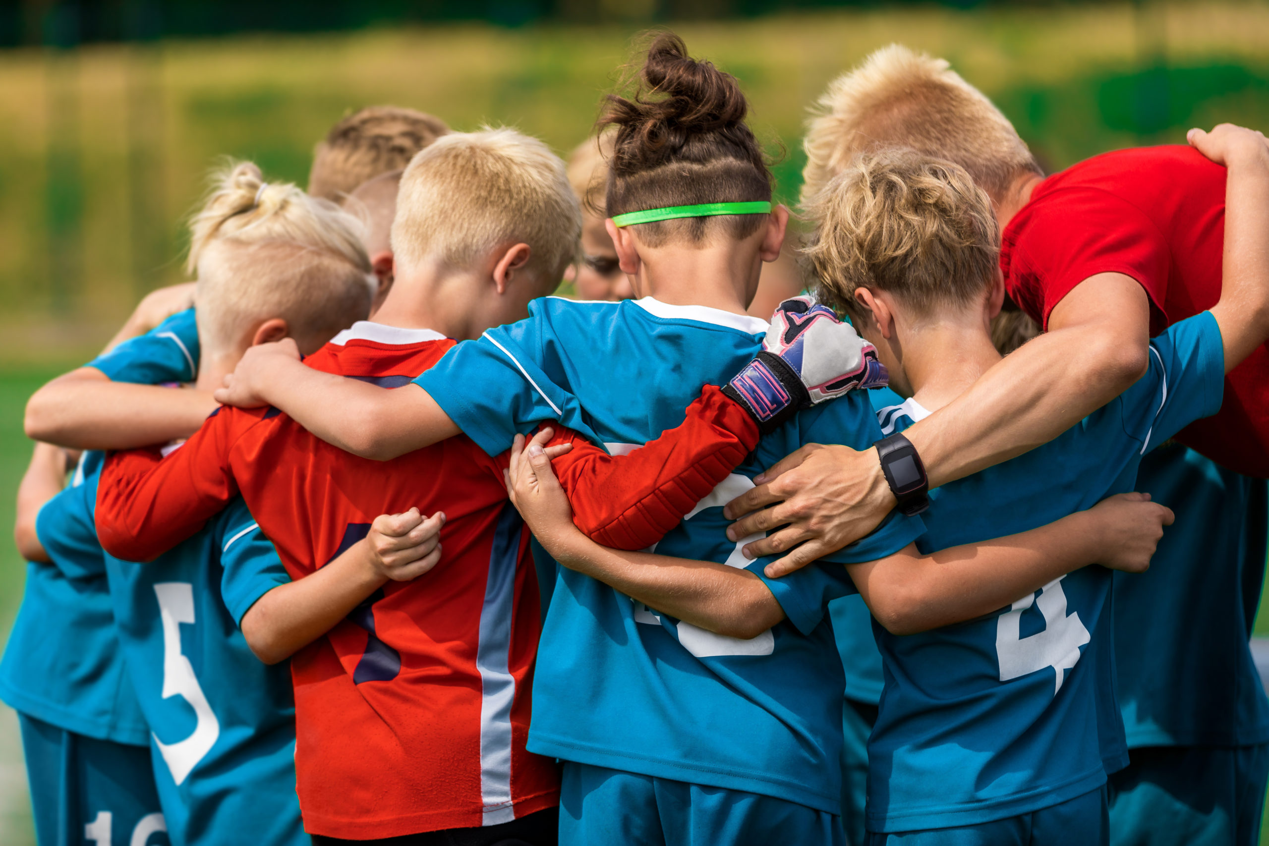 Youth soccer team huddled arm-in-arm in blue and red jerseys on a field