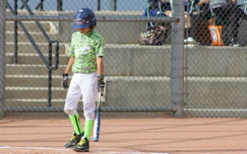 Young Baseball Batter At Plate Young baseball player in camo jersey and helmet standing at the plate holding a bat, head down