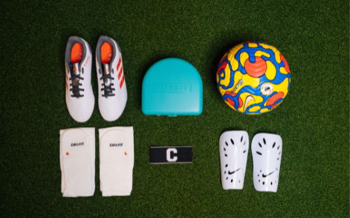 Soccer Gear Flat Lay Flat-lay of soccer gear on turf: cleats, shin guards, socks, ball, Trace device and captain armband