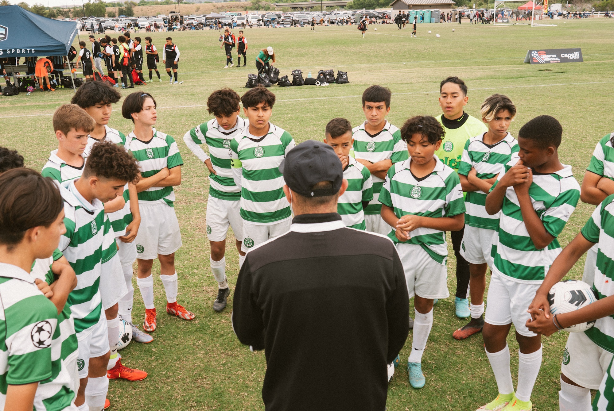 Coach addressing a youth boys team in green-and-white striped kits at a soccer tournament