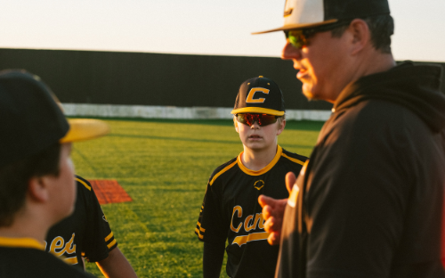 Coach Talking To Players Coach in sunglasses talking to young baseball players in black-and-gold uniforms at sunset
