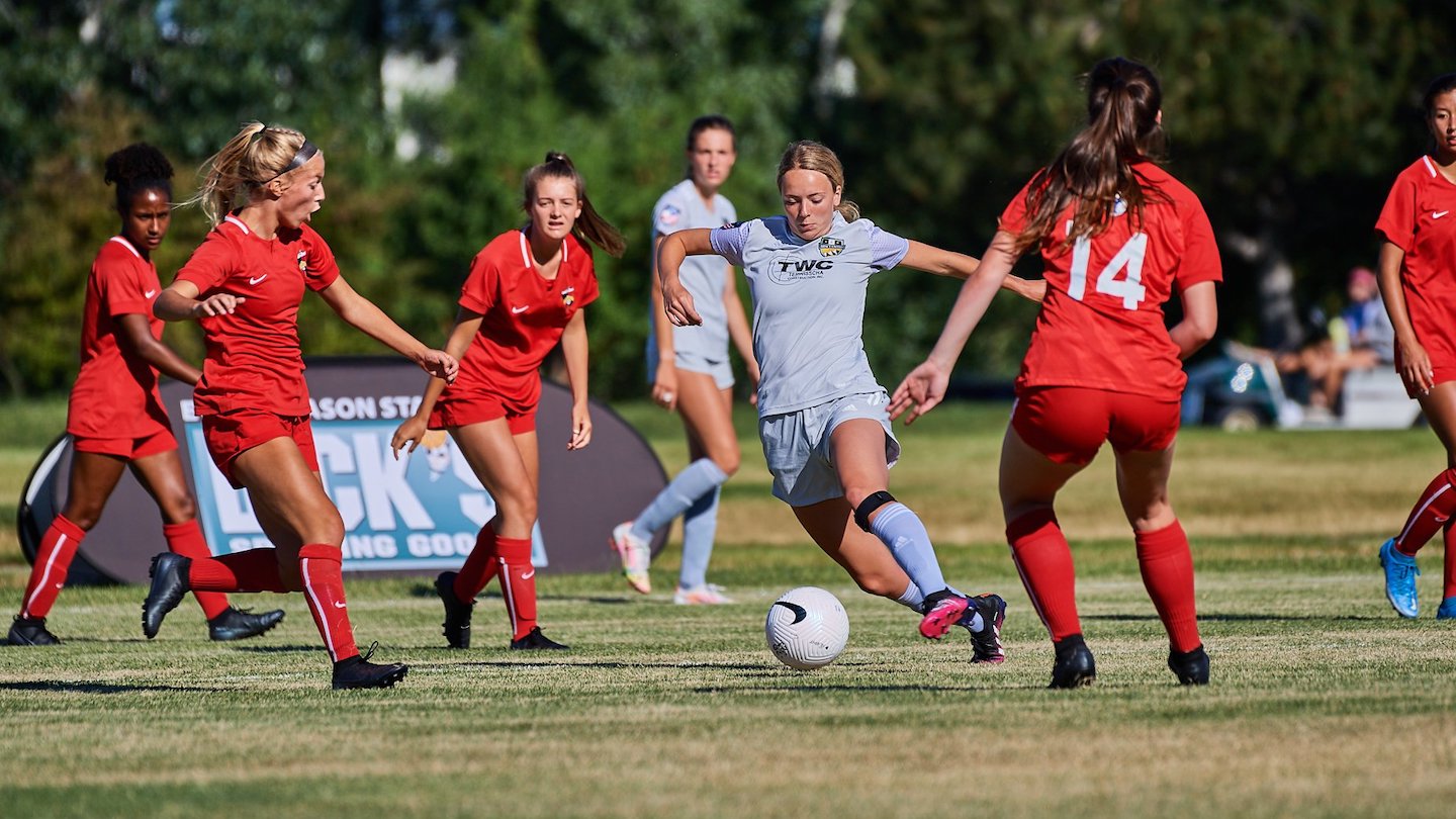 Female player in white dribbling the ball through a cluster of defenders in red jerseys during a match