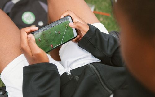 Overhead view of a young player watching a soccer match on a smartphone held sideways