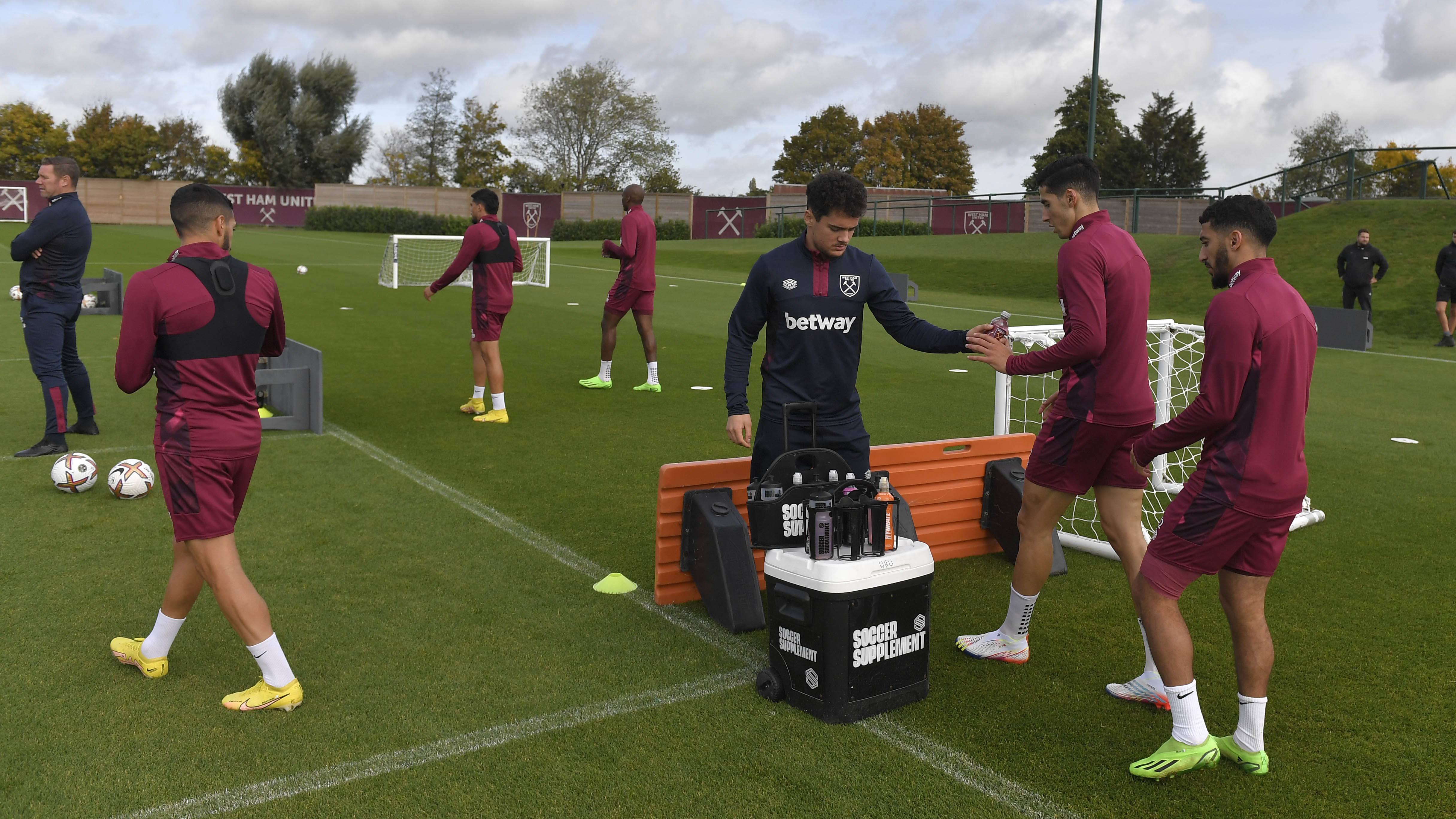 Players in maroon West Ham training kits doing drills near a water cooler on turf