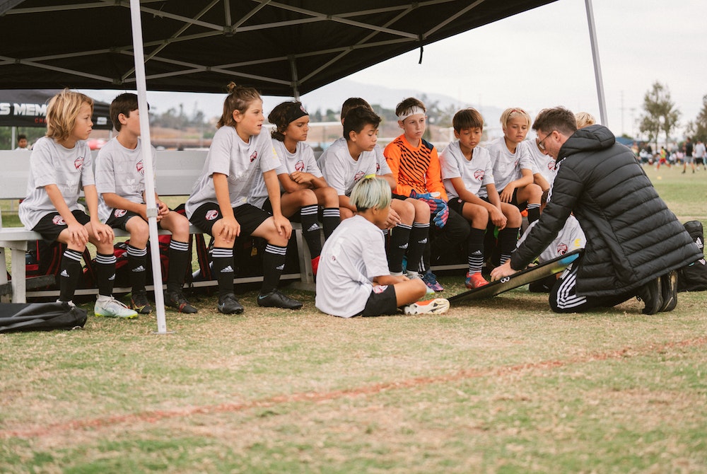 Coach Talking To Team Youth soccer team seated under a tent as a coach kneels talking to them