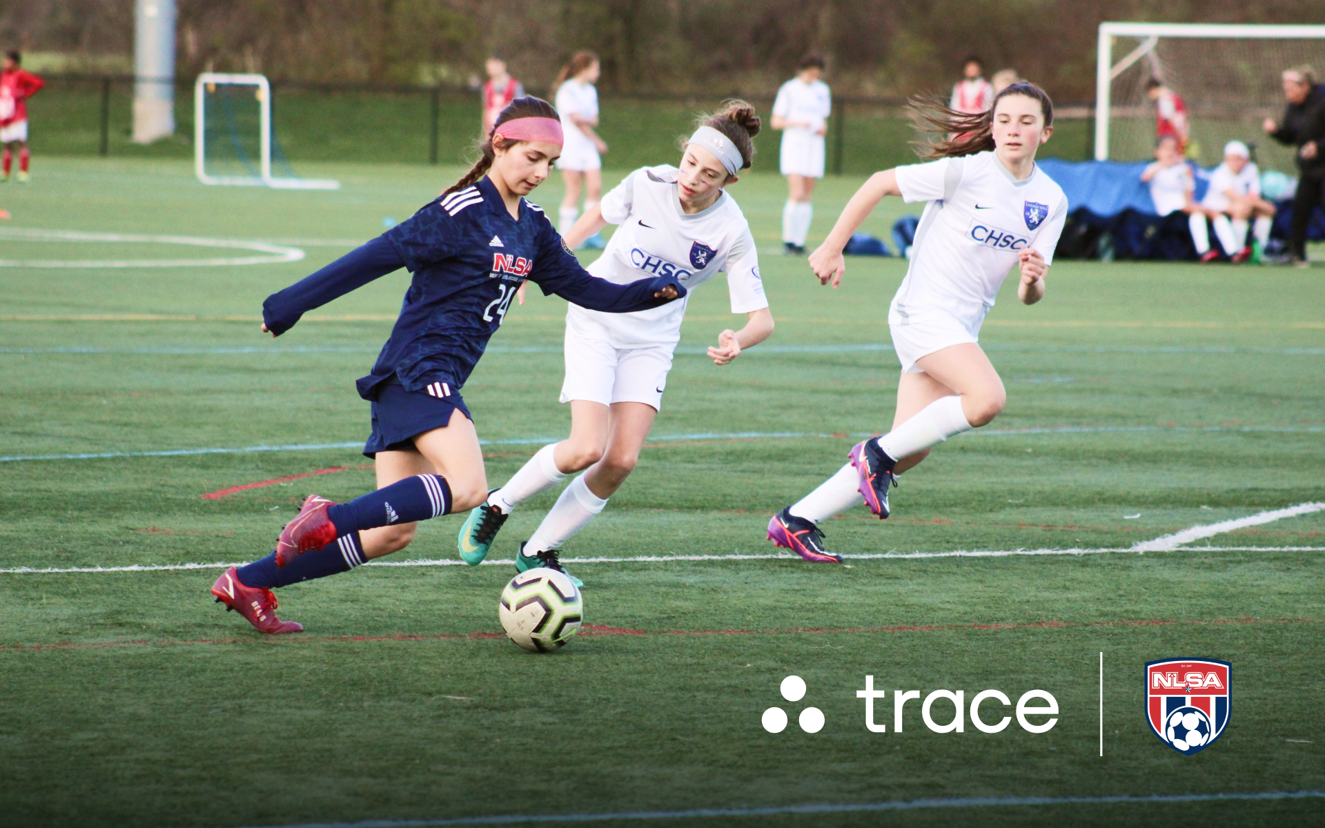Girls Soccer Match Action Girl in a navy NLSA kit dribbling past two white-kitted opponents, with Trace logos