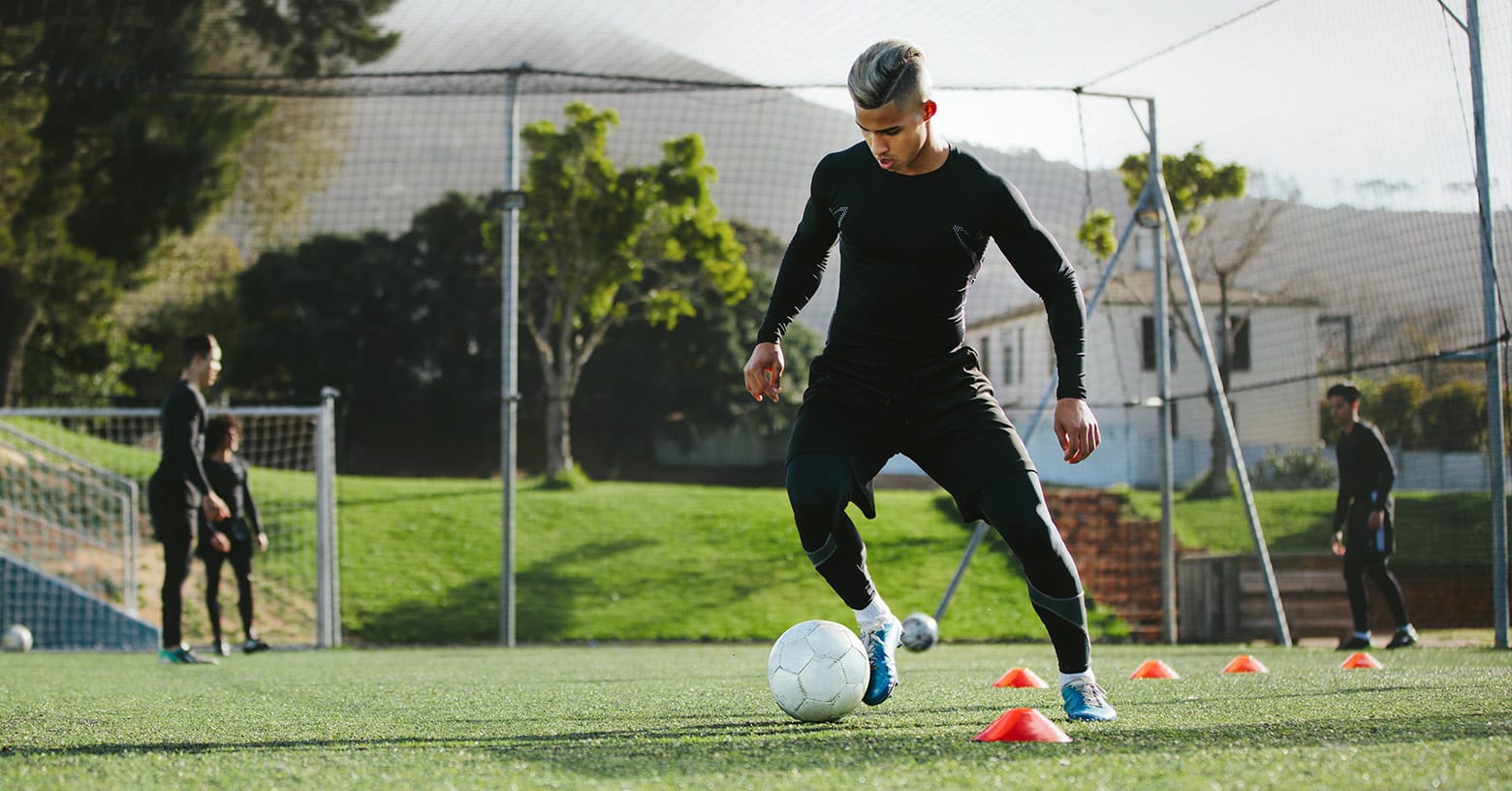 Player Dribbling Through Cones Young man in black training gear dribbling a soccer ball between cones on a field