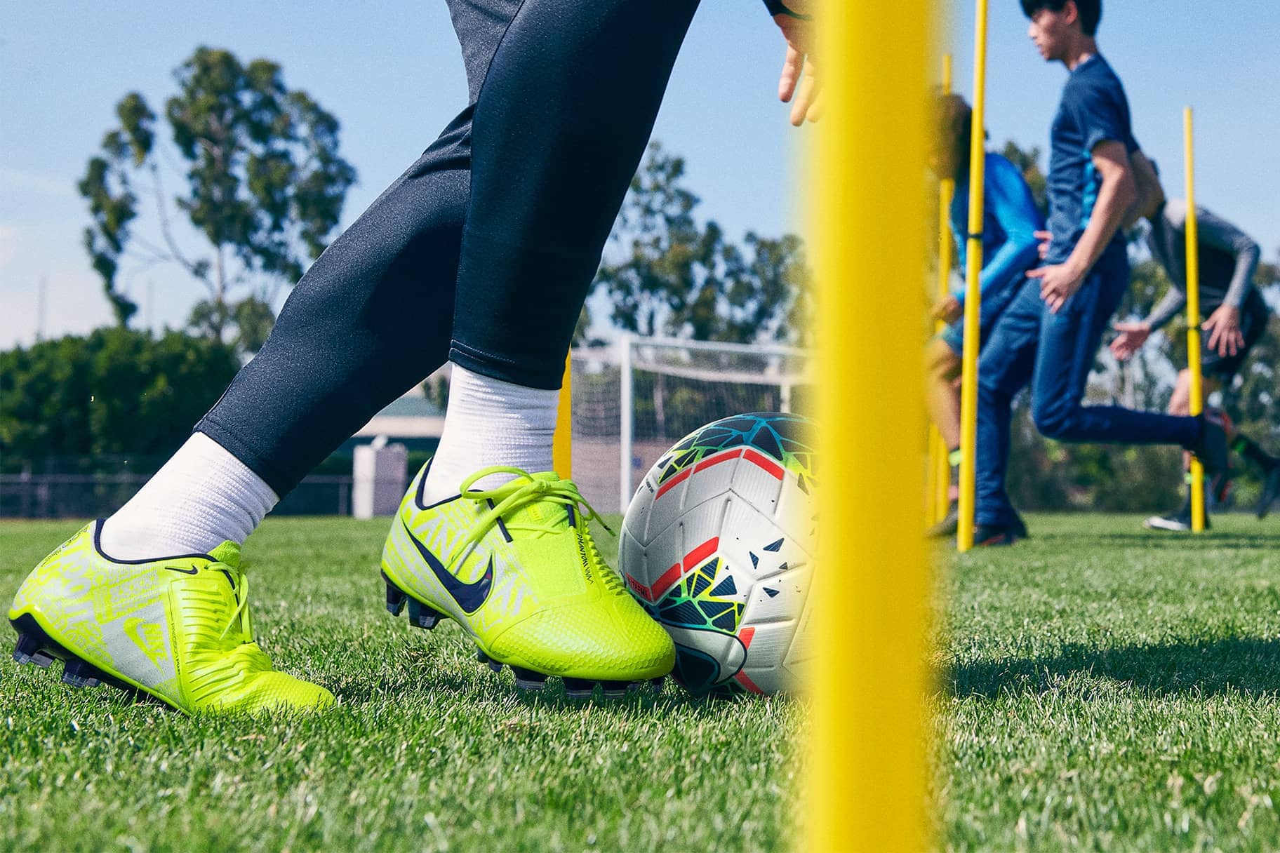 Neon Soccer Cleats Closeup Close-up of neon Nike soccer cleats beside a ball with agility poles on grass