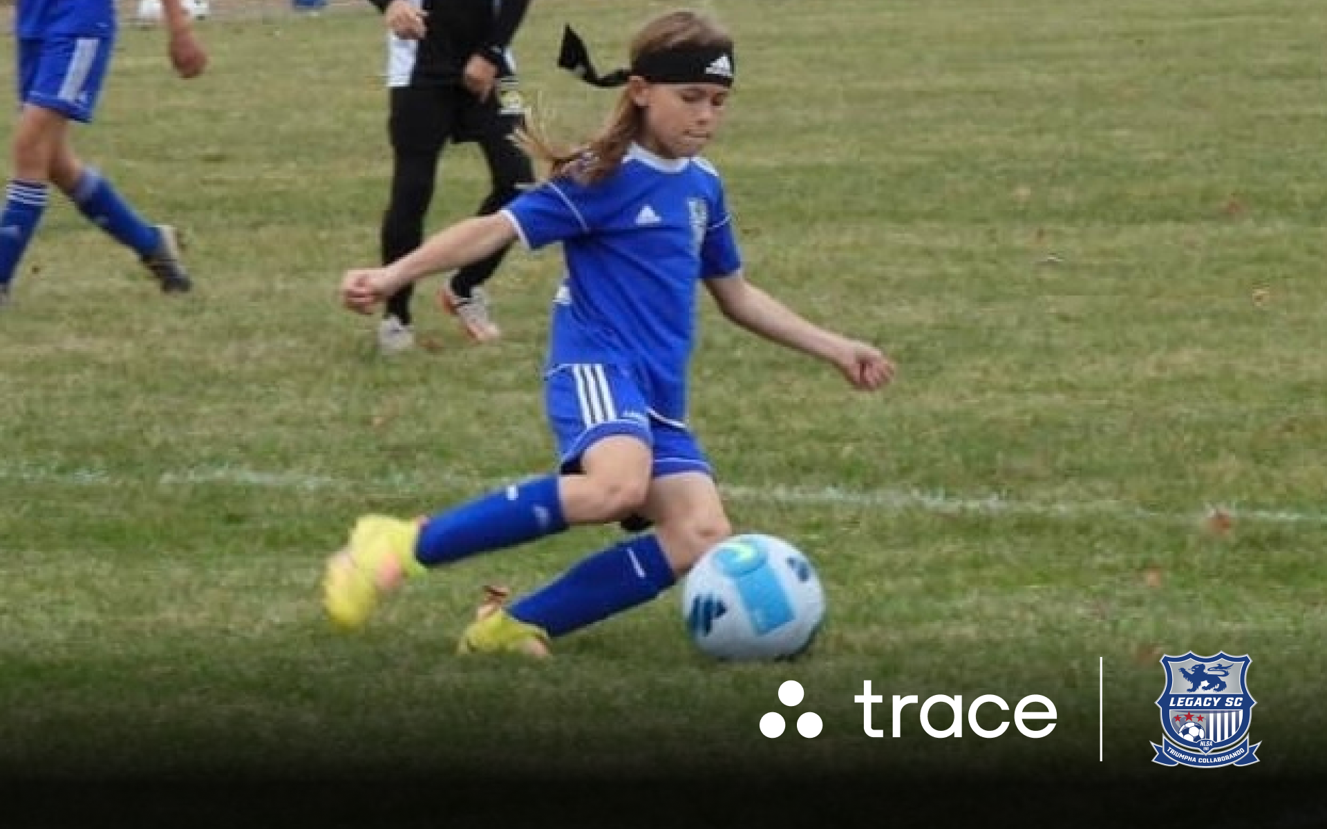 Young girl in a blue Legacy kit winding up to kick a ball, with Trace logos
