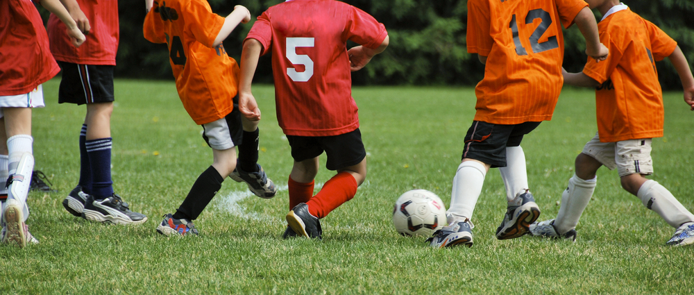 Kids Chasing Soccer Ball Young children in red and orange jerseys chasing a soccer ball during a game