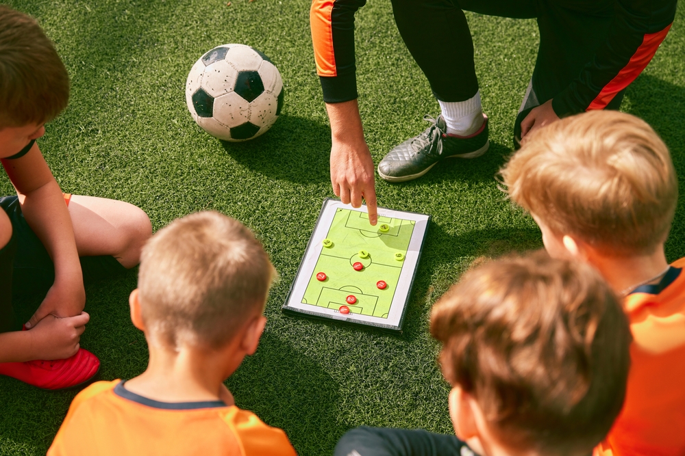 Coach Explaining Tactics Board Overhead view of a coach pointing at a tactics board surrounded by seated youth players