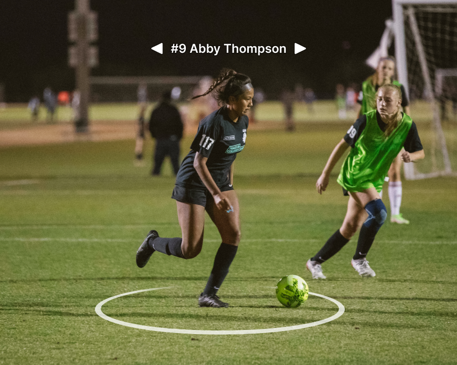 Player Highlight On Field Girl soccer player dribbling the ball at night past a defender, labeled #9 Abby Thompson.