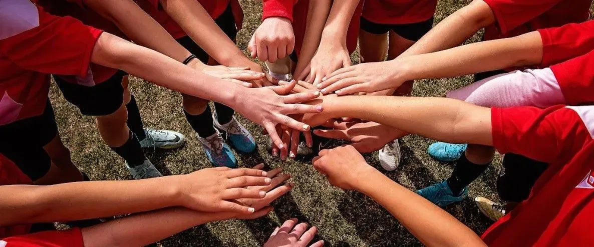 Top-down view of a youth soccer team stacking their hands together in a pregame huddle.
