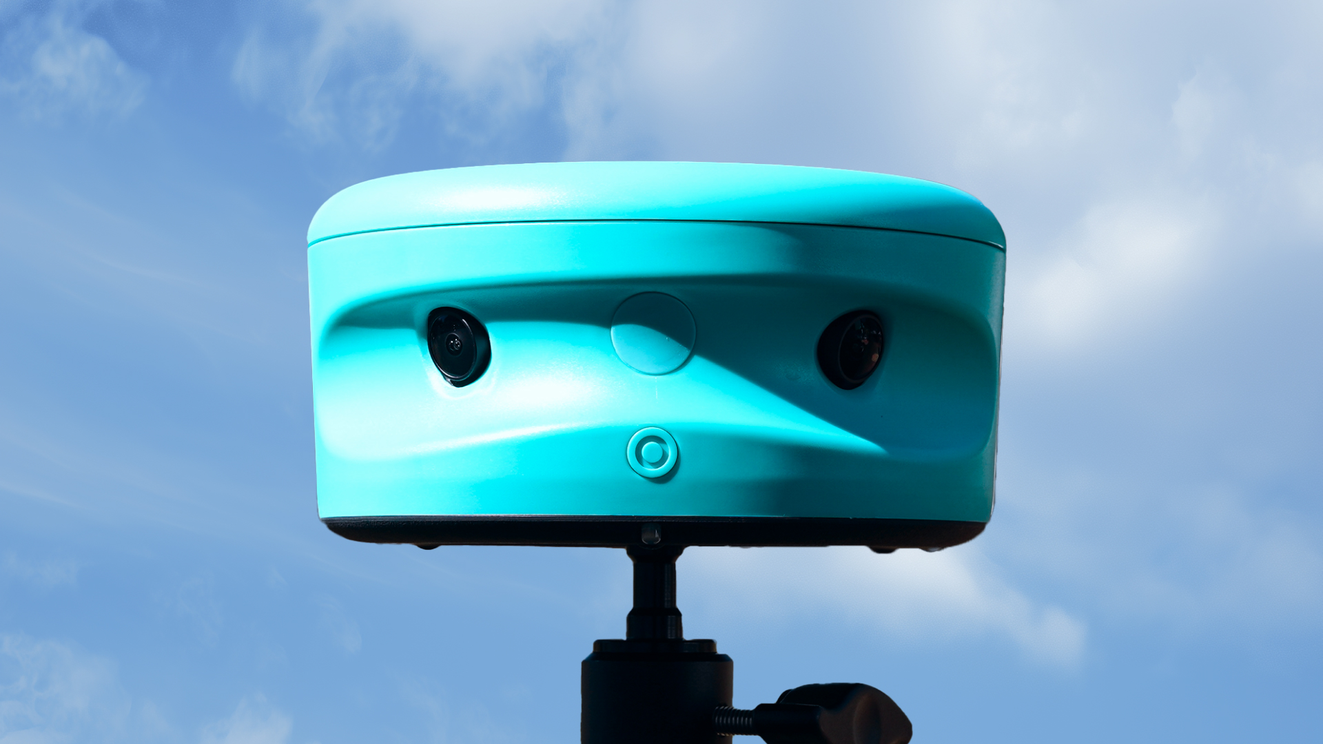 Teal Trace soccer camera mounted on a tripod against a blue, partly cloudy sky.