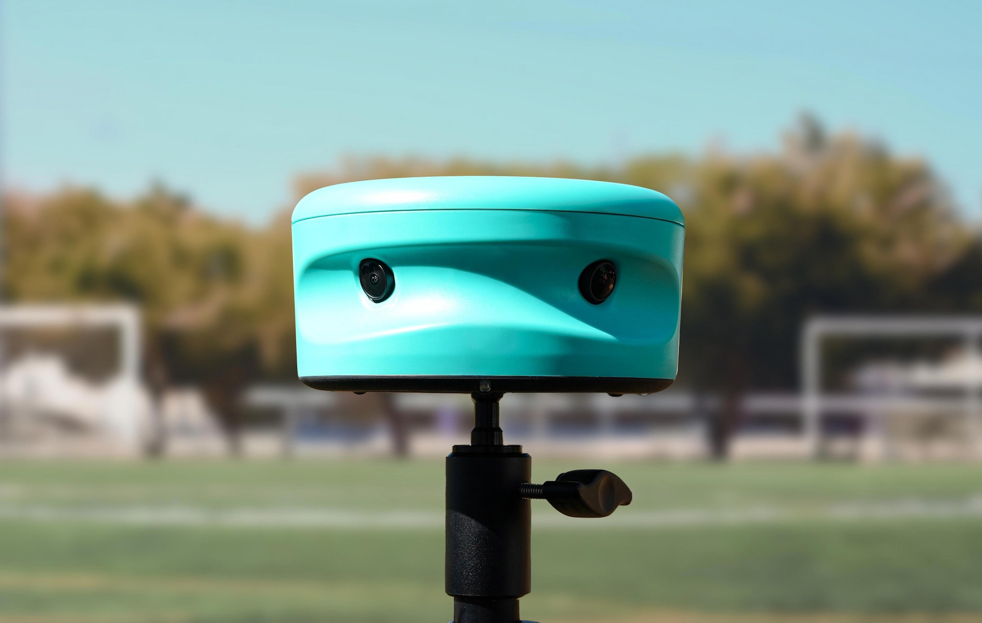 Teal Trace camera mounted on a tripod with a blurred soccer field and goals in the background